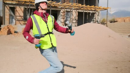 In front of an unfinished building, a funny man in construction gear grooves to the music with playful rhythm and visible delight, a lazy slacker breaking free from routine.