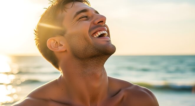 Handsome young man laughing with pure joy on a sunny beach, basking in the warm golden light of sunset.