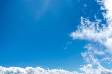 A serene blue sky dotted with fluffy white clouds stretches endlessly, creating a tranquil...