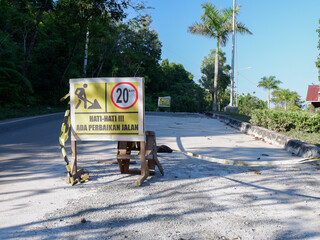 banner with the words HATI-HATI ADA PERBAIKAN JALAN in English, be careful, there are road repairs....