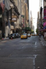 Yellow taxi cab is driving down flat design urban street, with traffic cone, signage, American flag