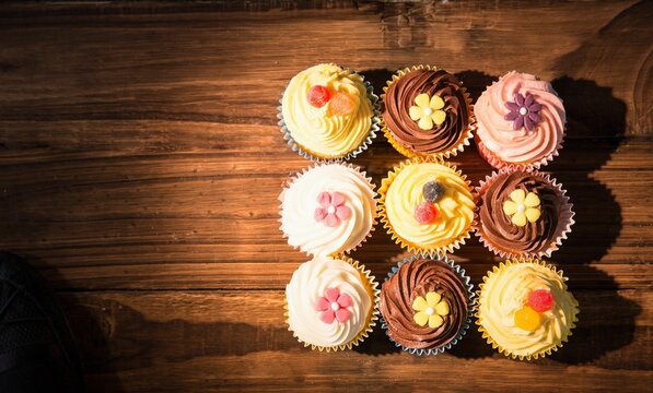 Naklejki Flat design showing nine pastel frosted cupcakes with candy gems on wooden table with warm lighting
