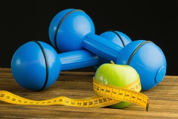 Blue dumbbells with green apple and measuring tape