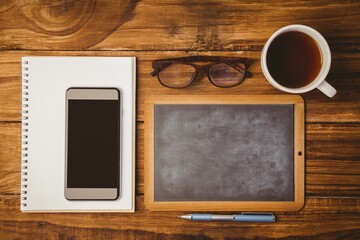 Showing flat-design overhead desk with pad and smartphone, framed chalkboard, glasses, coffee, pen