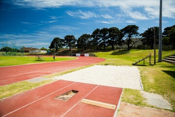 Long jump runway and sandpit are stretching across grassy field in flat design, showing red track