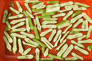 Freshly cut green sword bean slices in a red tray, ready for processing.