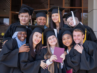 Happy students of different nationalities in graduation gowns hold their diplomas.