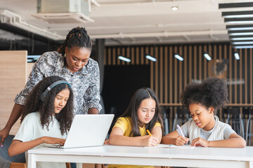 Diverse Group of Girls Learning with Teacher in Modern Classroom, Teacher Mentoring Young Students, Kids Using Laptop and Notebooks Under Teacher's Guidance in School