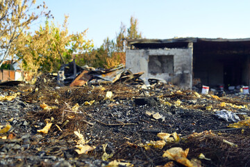 Burnt building ruins and charred debris after a devastating fire. Blackened ground, scorched trees,...
