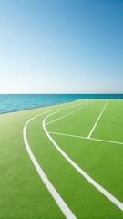 Obraz premium A vibrant green running track with white lanes curves along the edge of a tranquil blue ocean under a clear sky