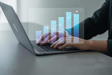 Close up of hands typing on a laptop keyboard with a futuristic holographic financial growth chart overlay