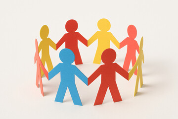 Group of paper figures in blue, red, yellow, standing in a circle holding hands, symbol of unity and collaboration, isolated on cream color background