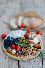 Wooden tray with delicious variety of cheese, nuts, olives, blueberries and strawberries, enjoying...