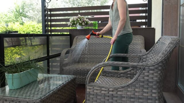 Anonymous cleaning, hose water washing wicker furniture from summer. Structures in backyard. Cleanliness and order.