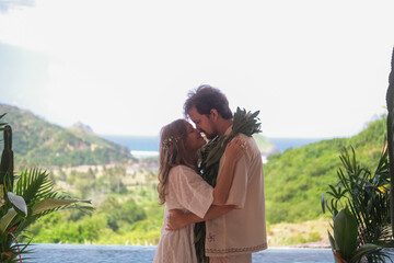 Outdoor wedding ceremony with ocean and green hills in the background. Bride in white dress and...