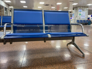Two blue metal-framed airport seats are positioned in a spacious terminal. The floor features a...