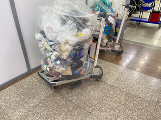 A cart filled with a large, transparent plastic bag overflowing with assorted waste items,...