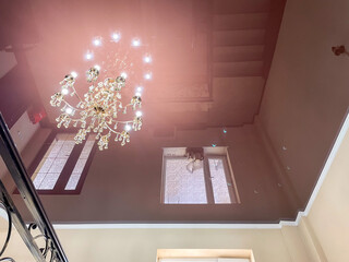 A stunning chandelier hangs from a glossy ceiling, reflecting light and creating intricate...