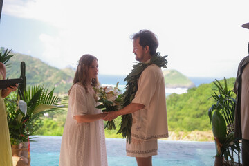 Outdoor wedding ceremony with ocean and green hills in the background. Bride in white dress and...
