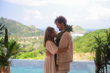 Outdoor wedding ceremony with ocean and green hills in the background. Bride in white dress and...