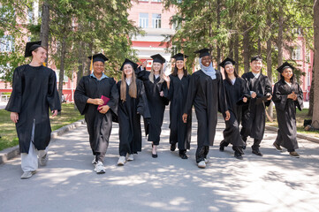 Students of different nationalities in graduation gowns walk through campus. 
