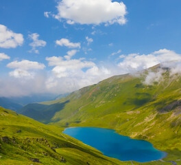 small lake in green mountain valley bowl in dense mist and clouds