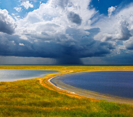 small lake among green prairie under a dense dramatic clouds
