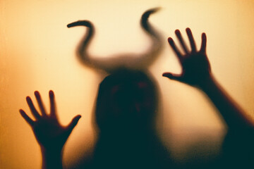 Horror, halloween background - Shadowy figure with horns behind the glass