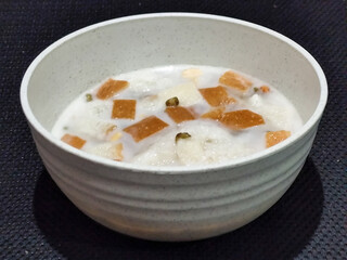 A large bowl of warm angsle, filled with slices of white bread, green beans, white sticky rice and...