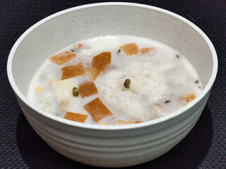 A large bowl of warm angsle, filled with slices of white bread, green beans, white sticky rice and...