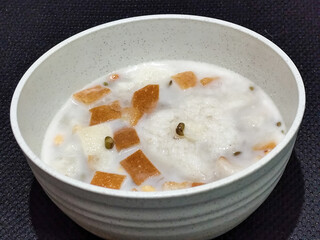 A large bowl of warm angsle, filled with slices of white bread, green beans, white sticky rice and pearls, sprinkled with warm, savory coconut milk sauce, traditional Indonesian food.