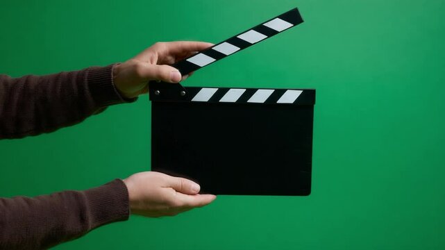 Clapperboard Moment: Hands holding a classic clapperboard against a vibrant green backdrop, capturing the beginning of a film production. A visual metaphor for filmmaking.