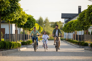 Fototapeta premium Family bike ride along tree-lined path near modern houses