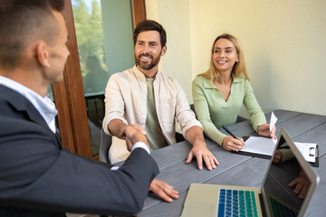 Real estate agent finalizing property contract with couple at outdoor table with laptop and...