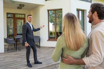 Real estate agent presenting house to couple outside property