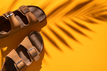 Brown sandals made of genuine leather on cork sole and shadow of tropical leaf on yellow background. Summer stylish fashion unisex shoes, beach casual flip flops. Minimalistic shoes background 