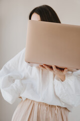 Elegant lady concealing features with laptop screen in neutral outfit. Minimalist fashion and...