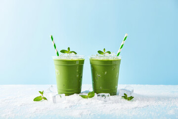 Two green smoothies with mint garnish and striped straws on a white surface against a blue backdrop