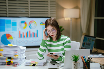 A stressed woman works late at a cluttered desk, surrounded by papers and charts, overwhelmed with...