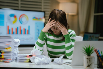 A stressed woman works late at a cluttered desk, surrounded by papers and charts, overwhelmed with...