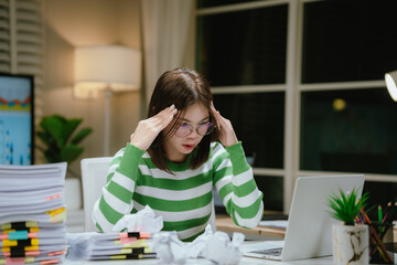 A stressed woman works late at a cluttered desk, surrounded by papers and charts, overwhelmed with...
