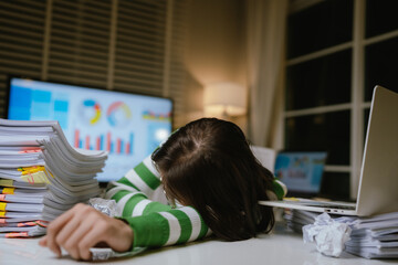 A stressed woman works late at a cluttered desk, surrounded by papers and charts, overwhelmed with...