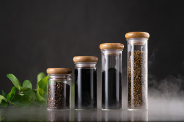 Glass jars with wooden lids filled with spices and herbs on a reflective surface and dark background