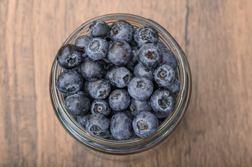 A jar filled with blueberries stands on a wooden table, pattern, top view