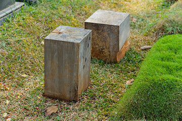 Two square wooden beams are placed on a grassy ground in an open area, featuring natural textures and a rustic outdoor atmosphere. Suitable for nature themes or traditional constructions.