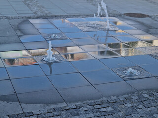 square granite paving stacked in a strip in sidewalk,boy, water sprays with alternating spray...