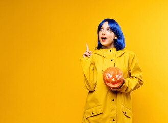 Young girl wearing yellow jacket hold halloween pumpkin jack o lantern and point finger on yellow...