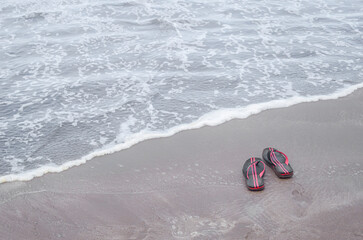 Flip-flops resting on sandy beach with ocean waves gently crashing in background