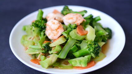 table top view stir-fried broccoli with shrimp and carrot in white plate isolated on black background.