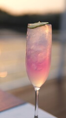A glass of pink champagne with ice cubes on a blurred background.